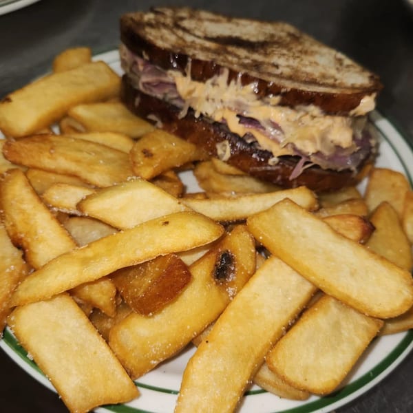 A close-up of a hearty sandwich with melted cheese and red onions, served with golden fries.